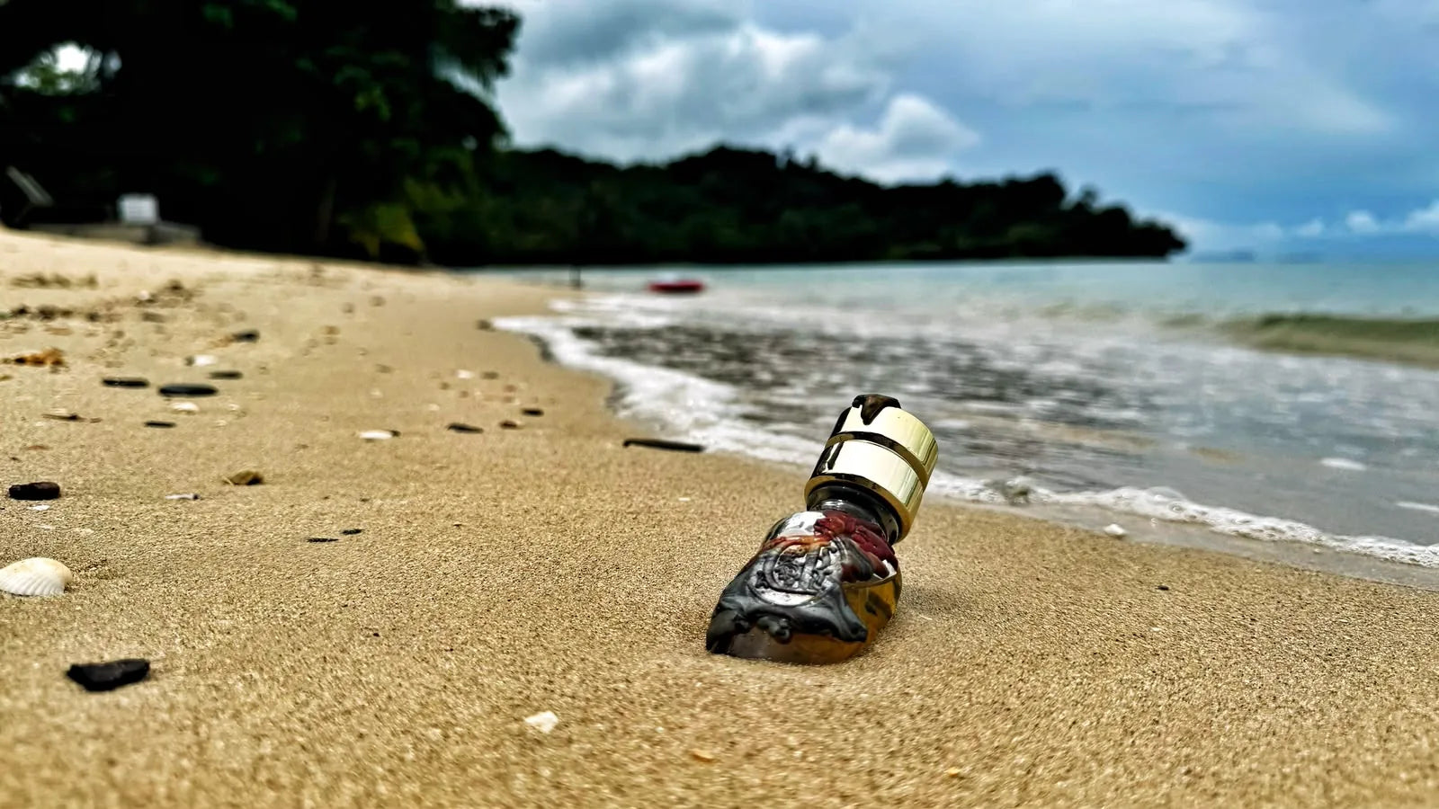 Ein versiegelter Duftkumpels-Flakon im Sand an einem Strand in Thailand